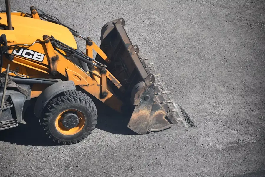 Yellow backhoe loader digging into gravel in daylight